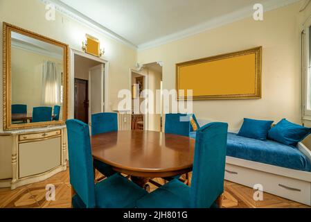 Soggiorno di una casa con tavolo da pranzo in legno con sedie blu imbottite e un divano letto con tappezzeria coordinata Foto Stock