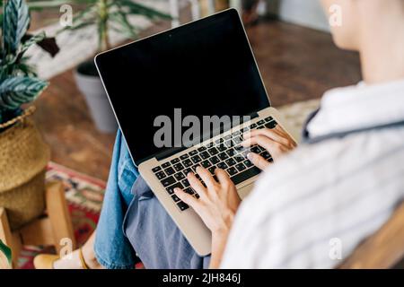Primo piano di un notebook sul grembo di una donna d'affari irriconoscibile che digita su una tastiera. Foto Stock