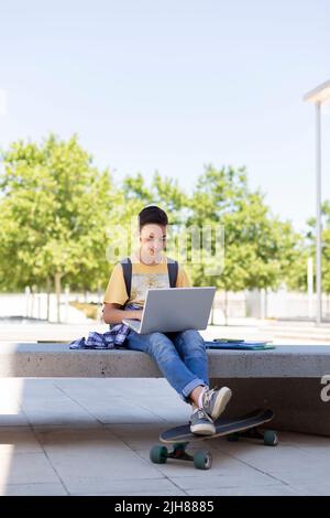 Adolescente caucasico che usa il computer portatile all'aperto. Torna a scuola. Spazio per il testo. Foto Stock