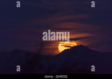 Grande luna Harvest che sorge sulle montagne dell'Arizona, parzialmente ricoperta da nuvole Foto Stock