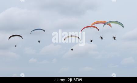 Un gruppo di colorati parapendio motorizzati che volano nel cielo blu con le nuvole sullo sfondo Foto Stock