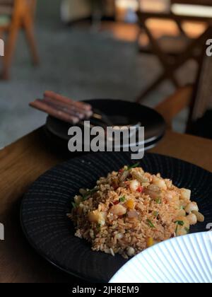 Un colpo verticale di riso fritto con gamberi tritati e verdure su un piatto nero Foto Stock