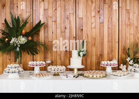 Una torta e un dessert su un tavolo contro una parete di legno in un matrimonio a tema tropicale Foto Stock