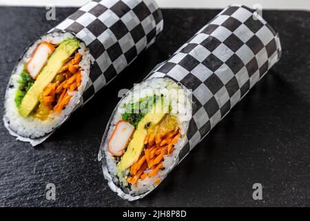 Due pezzi di sushi burritos su un asse di legno nero Foto Stock