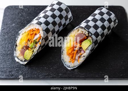 Due pezzi di sushi burritos su un asse di legno nero Foto Stock