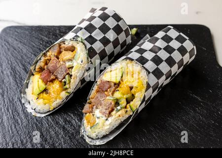 Due pezzi di sushi burritos su un asse di legno nero Foto Stock