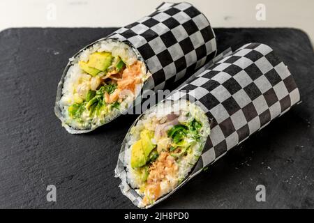 Due pezzi di sushi burritos su un asse di legno nero Foto Stock