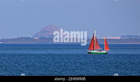 Portobello, Edimburgo, Scozia, Regno Unito 16th luglio 2022. Il sole del pomeriggio è scoppiato dopo una mattinata molto nuvolosa, la temperatura di 22 gradi centigradi ha portato fuori uno yacht a vela sul Firth of Forth con il suo caldo torbido e la legge di Berwick nel backgound. Foto Stock