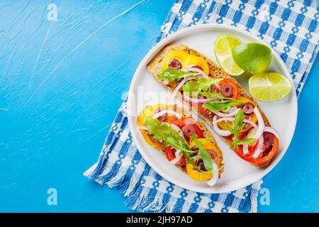 Tapas spagnole tradizionali su sfondo blu. Panini sani con verdure, verdure, olive e lime. Sandwich vegetariani su un piatto bianco. T Foto Stock