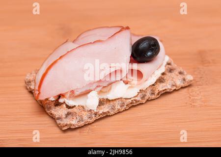 Crospead di grano intero con prosciutto, formaggio cremoso e olive sul tagliere di bambù. Colazione facile. Dieta alimentare. Panini veloci e sani. Croccante con gustoso ripieno. Snack dietetico sano Foto Stock