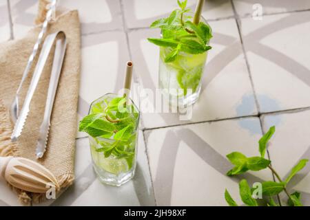 Mojito e accessori bar su una piastrella. Due bicchieri di mojito cocktail con menta e lime. Cocktail estivo con paglia di bambù Foto Stock