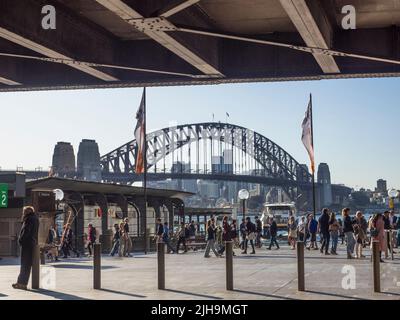 I turisti si recano intorno a Circular Quay con il Sydney Harbour Bridge e North Sydney sullo sfondo. Il collegamento City Rail passa in alto. Foto Stock