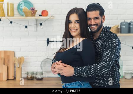 Primo piano medio di felice coppia eterosessuale che si abbracciano in cucina. Orgoglioso marito bearded dai capelli scuri sta andando essere un padre. Inizio della gravidanza. Foto di alta qualità Foto Stock
