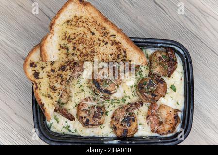 Vista dall'alto di una cheesy ciotola di gamberi alfredo servita in un contenitore da togliere con due fette di pane tostato all'aglio. Foto Stock