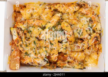 Vista dall'alto di un abbondante ordine laterale di patatine fritte di pollo di bufala coperte di formaggio e servite in una scatola da aspire per mangiare in movimento. Foto Stock