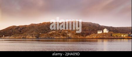 Paesaggio marino vicino a una montagna con case su una collina. L'oceano o un grande lago con edifici residenziali in lontananza all'aperto durante il tramonto su un Foto Stock