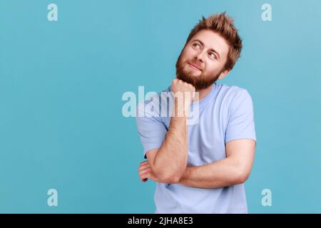 Ritratto di uomo sorridente e felice che guarda via con espressione pensiva, sognando pensieri piacevoli, fantasizzando e facendo il desiderio. Studio interno girato isolato su sfondo blu. Foto Stock