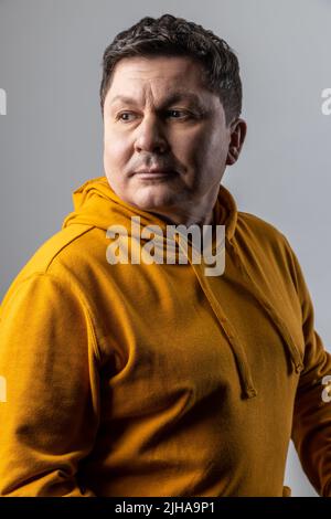 Ritratto di bel pensivo uomo di mezza età guardando pensivo pensieroso, guardando via, essendo profondo nei pensieri, indossando la felpa con cappuccio di stile urbano. Studio interno girato isolato su sfondo grigio. Foto Stock