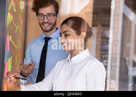 Colleghi di affari felici e diversi che discutono le mansioni di progetto alle note adesive Foto Stock