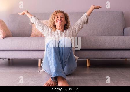 Donna felice e soddisfatto a casa seduta sul pavimento braccia aperte e sorridente. Concetto di gioioso stile di vita femminile. Attività ricreative al coperto, S Foto Stock