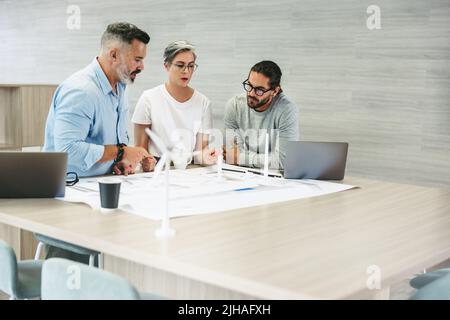 Tre professionisti del design creativo che lavorano con progetti di turbine eoliche in un ufficio moderno. Team di imprenditori innovativi brainstorming mentre wor Foto Stock