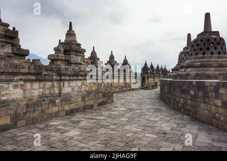 Interno dell'antico tempio Borobudur a Giava centrale, Indonesia. Corridoio vuoto sulla terrazza superiore con cielo blu nuvoloso. Nessuna gente. Foto Stock