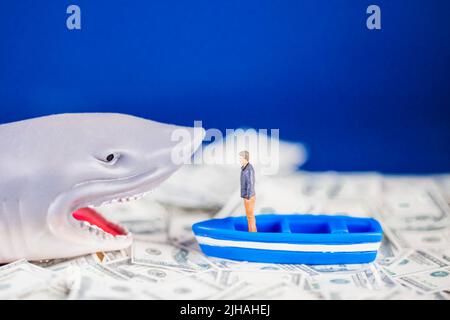Uomo in miniatura su una piccola barca blu di fronte a uno squalo prestito sul dollaro oceano. Concetto di squalo di prestito. Foto Stock