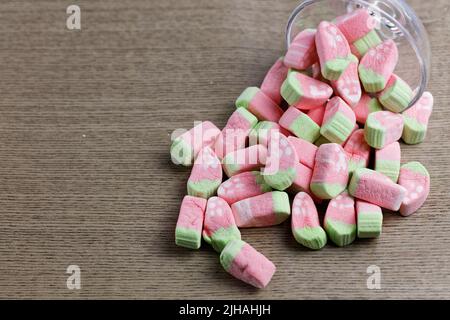 Marshmallows colorati in miniatura in un vetro versato su uno sfondo di legno Foto Stock