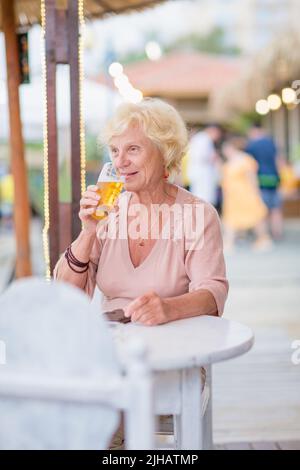 Donna matura seduta a un tavolo in un bar estivo e bere birra Foto Stock