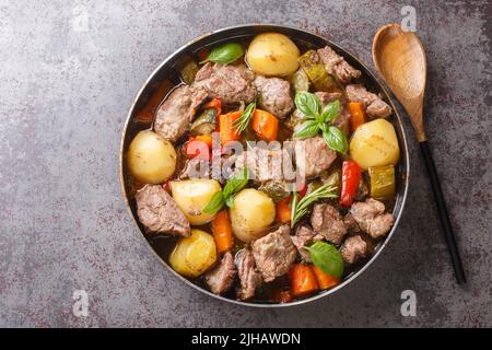 Piatto croato tradizionale vista Peka, carne e verdure in ferro coperchio sotto caldo bagliore primo piano sul tavolo. Vista orizzontale dall'alto Foto Stock