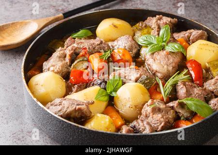 Piatto croato tradizionale vista Peka, carne e verdure in ferro coperchio sotto caldo bagliore primo piano sul tavolo. Orizzontale Foto Stock