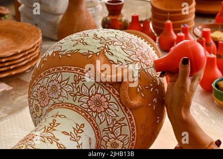 Rodi, Grecia - Maggio 2022: Vista ravvicinata di un artista di ceramica che usa la vernice liquida colorata per riempire un modello intricato su un vaso grande Foto Stock