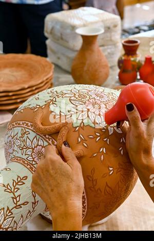 Rodi, Grecia - Maggio 2022: Vista ravvicinata di un artista di ceramica che usa la vernice liquida colorata per riempire un modello intricato su un vaso grande Foto Stock