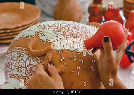 Rodi, Grecia - Maggio 2022: Vista ravvicinata di un artista di ceramica che usa la vernice liquida colorata per riempire un modello intricato su un vaso grande Foto Stock