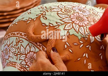 Rodi, Grecia - Maggio 2022: Vista ravvicinata di un artista di ceramica che usa la vernice liquida colorata per riempire un modello intricato su un vaso grande Foto Stock