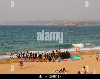 Un grande gruppo di surfisti in un semicerchio sulla spiaggia Sardinero Santander Cantabria Spagna in un semicerchio esercizi di riscaldamento durante una lezione Foto Stock