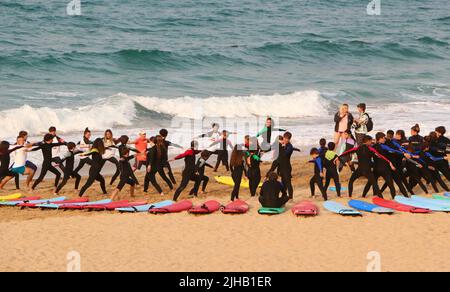 Un grande gruppo di surfisti in un semicerchio sulla spiaggia Sardinero Santander Cantabria Spagna in un semicerchio esercizi di riscaldamento durante una lezione Foto Stock