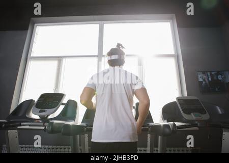 Inquadratura posteriore ad angolo basso di uno sportivo irriconoscibile che corre sullaammill Foto Stock