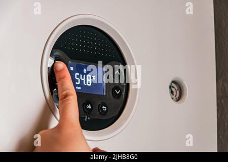 La mano femminile regola una caldaia a gas riscaldante a casa. L'immagine simbolica della stagione del riscaldamento a casa. Un'immagine concettuale per la bolletta del gas, il riscaldamento Foto Stock