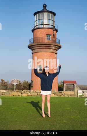 Una donna cinese che salta di fronte alla casa faro di Gayhead ad Aquinnah, Massachusetts, sul vigneto di Martha's. Foto Stock