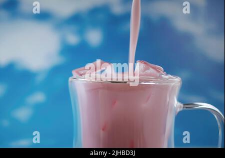 Primo piano tazza di vetro doppia con movimento versante di colore rosa pastello bevanda con sfondo cielo blu, tema pastello, movimento sfocato Foto Stock