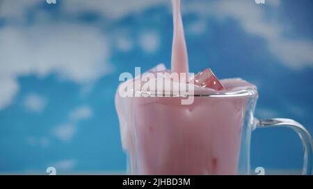 Primo piano tazza di vetro doppia con movimento versante di colore rosa pastello bevanda con sfondo cielo blu, tema pastello, movimento sfocato Foto Stock