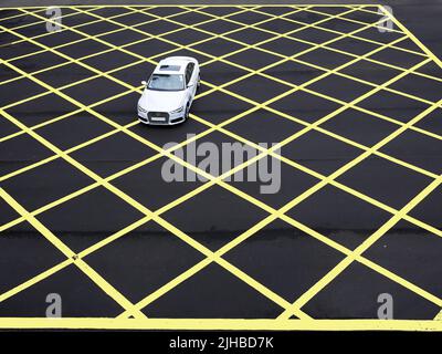 Un'auto passa attraverso la strada asfaltata che dipinse in linea gialla forma geometrica a griglia quadrata modello di linea di marcatura Foto Stock