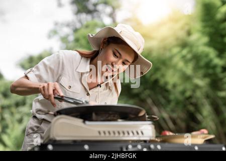 Giovane ragazza aisan grigliare barbecue nel campeggio durante il viaggio estivo campo, spiedini di maiale e filetto di manzo sul barbecue party in campeggio, Summer Camp Foto Stock