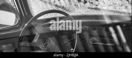 Un colpo panoramico bianco e nero dell'interno di una vecchia auto classica con parabrezza rotto Foto Stock