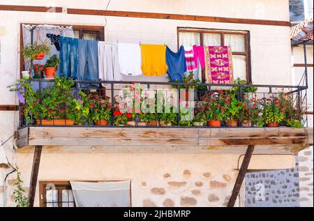 Fiori sul balcone di una vecchia casa e vestiti appesi su un filo Foto Stock