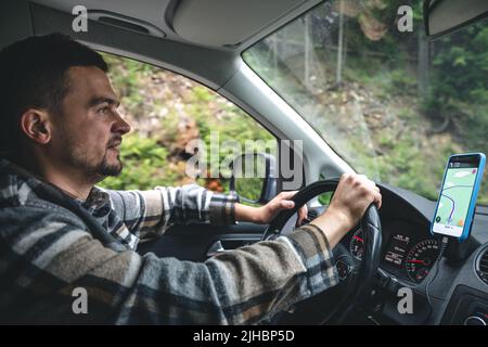 Un uomo che guida un'auto corre in un'area forestale montagnosa. Foto Stock