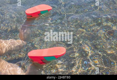 Vista ravvicinata delle gambe femminili in scarpe da nuoto rosse in acqua. Concetto di vacanza estiva. Foto Stock