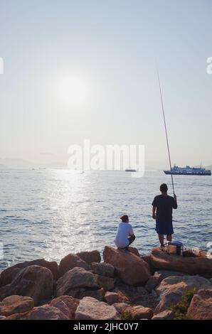 Un colpo verticale di due uomini che cercano di catturare il pesce con un cenno di pesca a Hong Kong Foto Stock