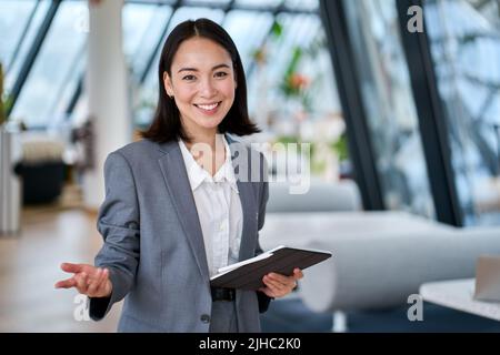 Allegro giovane donna di vendita asiatica che guarda la macchina fotografica che accoglie il cliente. Foto Stock